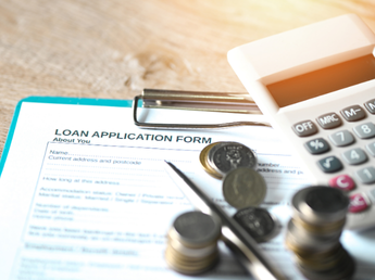 A loan application form placed on a table alongside scattered coins and a calculator, symbolizing financial planning and access to credit through NBFCs using Twinline.org's lending software.